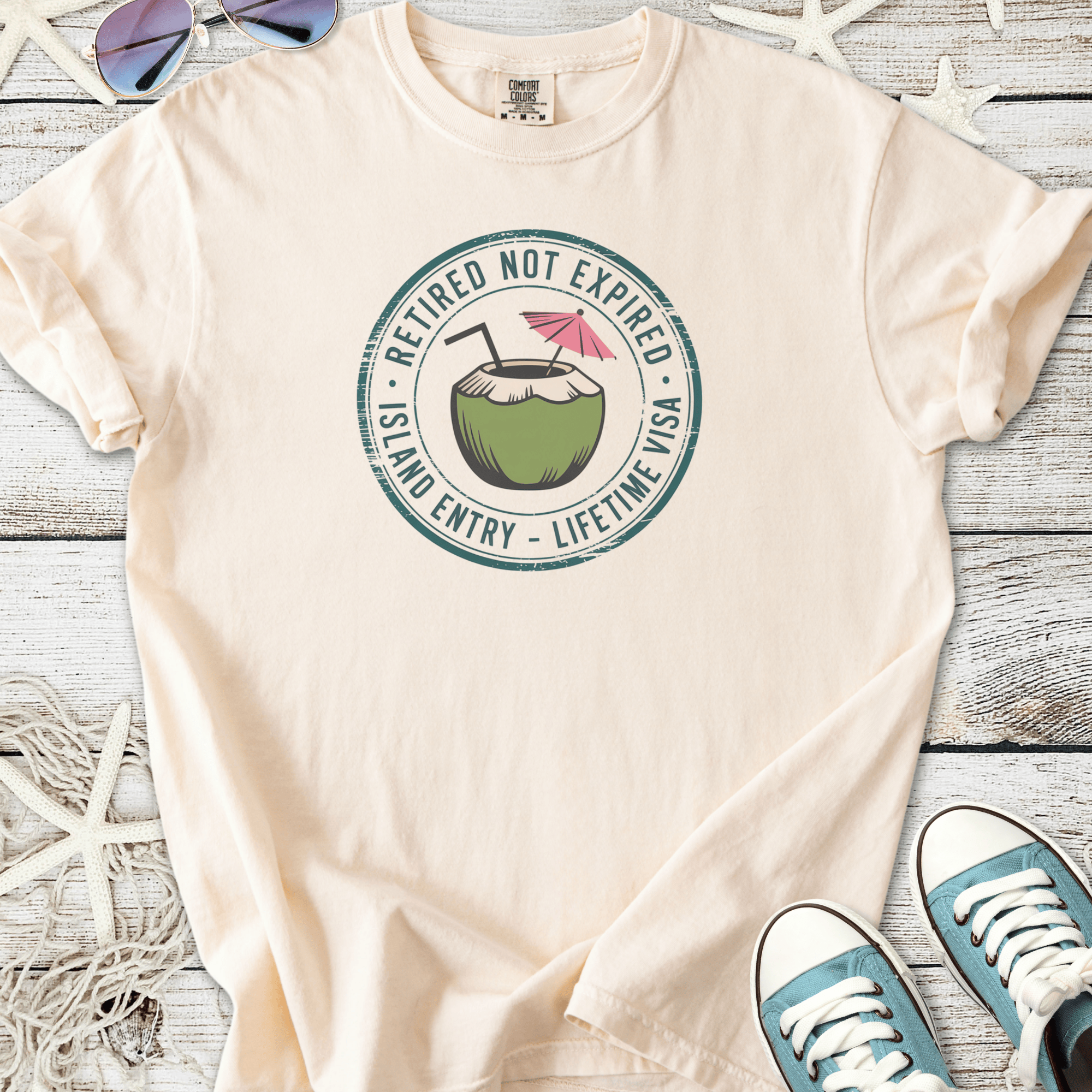 Cream retirement beach themed graphic t-shirt with coconut drink and ‘Retired Not Expired — Lifetime Visa’ text