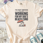 Cream graphic tee featuring a dog, beach umbrella, and text about dog fund, perfect for pet lovers.