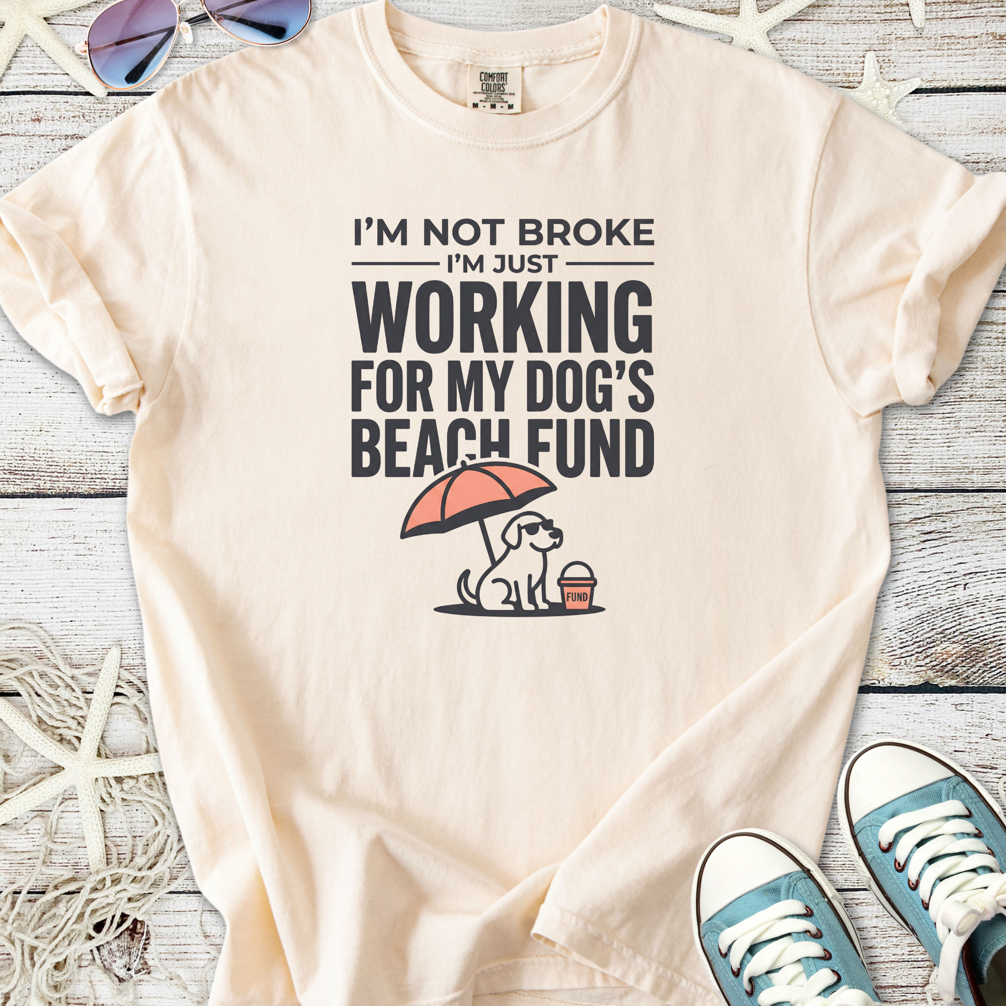 Cream graphic tee featuring a dog, beach umbrella, and text about dog fund, perfect for pet lovers.