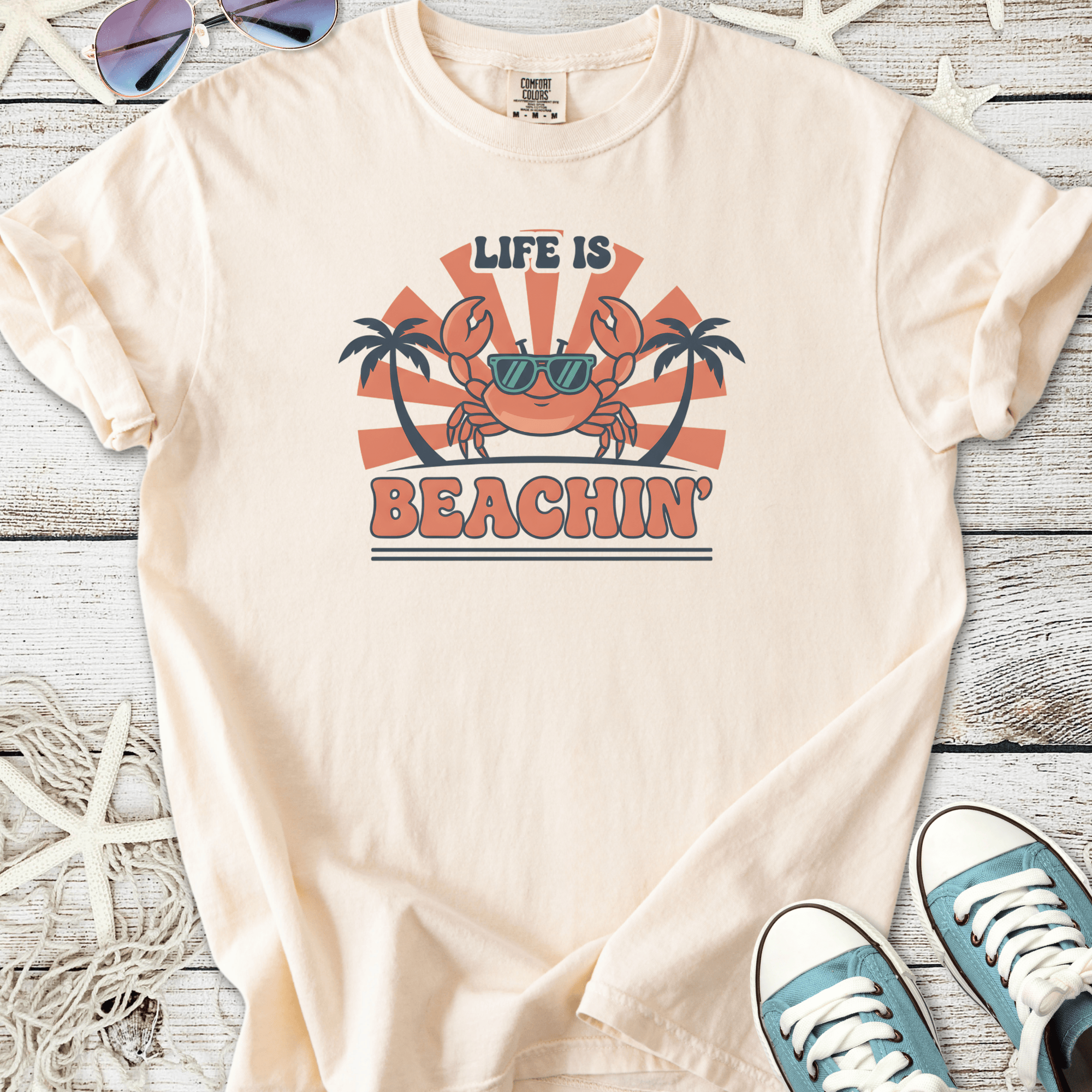 Light beige t-shirt featuring a fun crab graphic with sunglasses, text 'Life is Beachin', perfect for summer wear.
