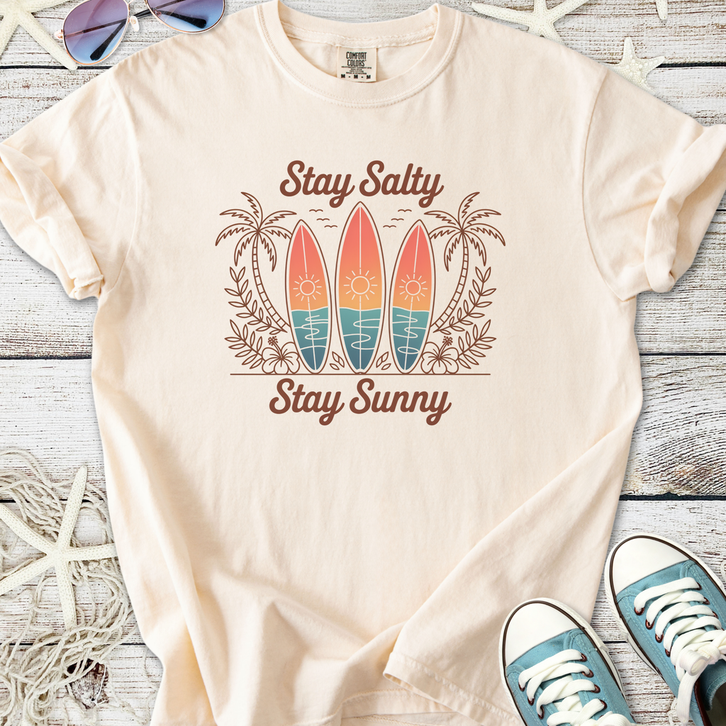 Beige graphic t-shirt featuring surfboards, palm trees, and the text 'Stay Salty Stay Sunny'