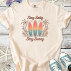 Beige graphic t-shirt featuring surfboards, palm trees, and the text 'Stay Salty Stay Sunny'