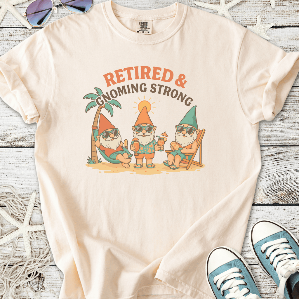 Cream t-shirt featuring three gnomes with sunglasses in a beach setting, saying 'Retired & Gnoming Strong'.