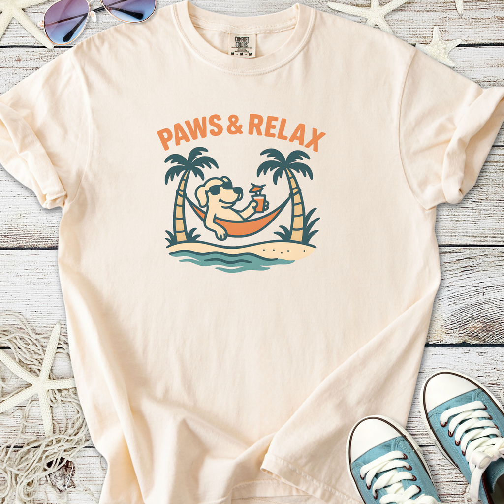 Light peach t-shirt with 'Paws & Relax' graphic featuring a dog on a hammock surrounded by palm trees.