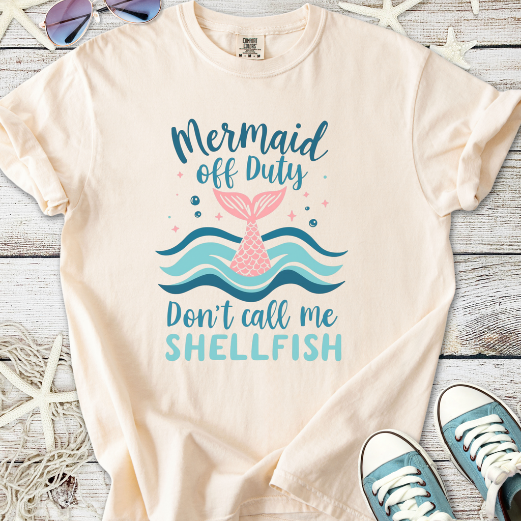Cream beach themed graphic t-shirt with mermaid tail, ocean waves, and ‘Mermaid Off Duty — Don’t Call Me Shellfish’ text