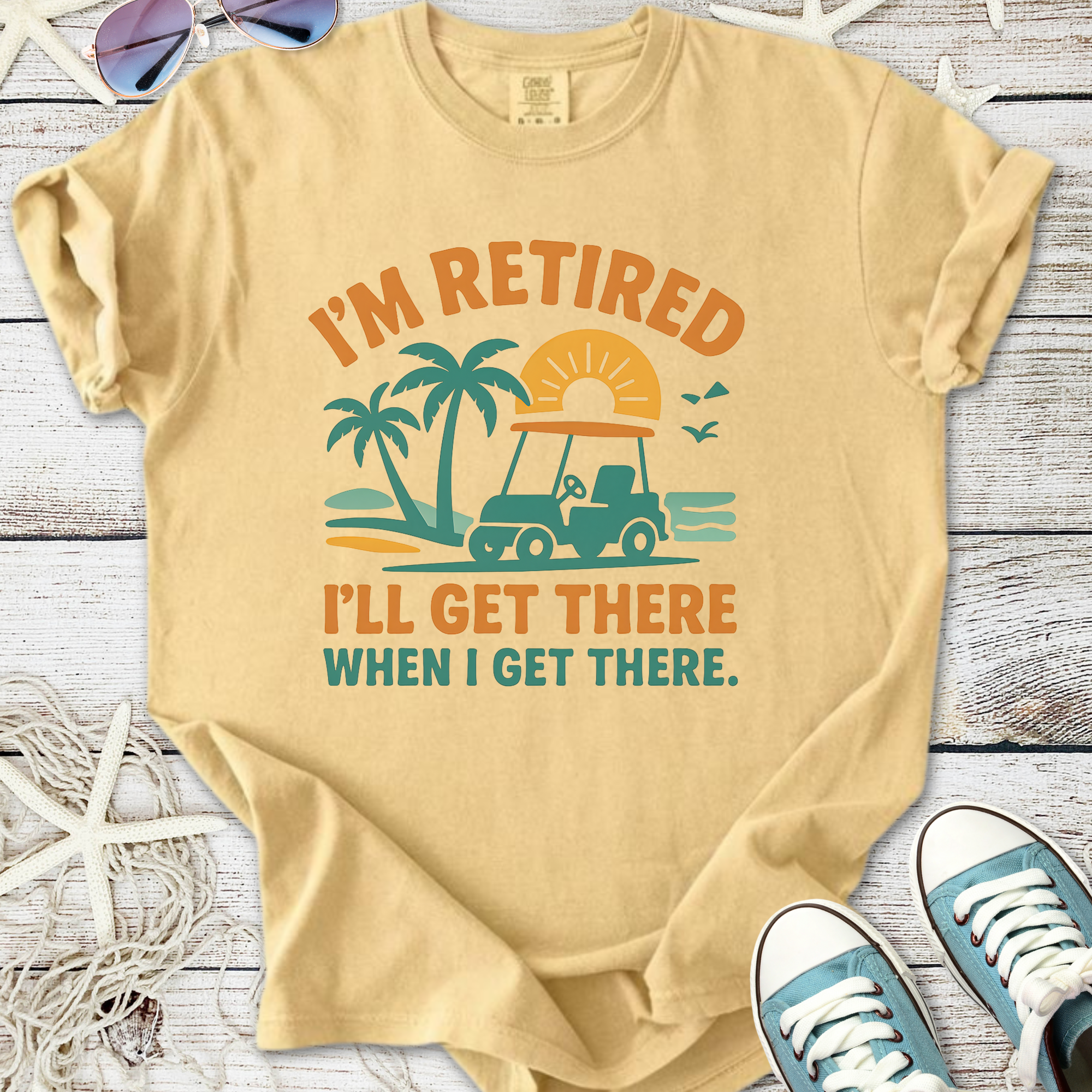 Beige retired graphic t-shirt featuring a golf cart, palm trees, and sunset design for casual wear.
