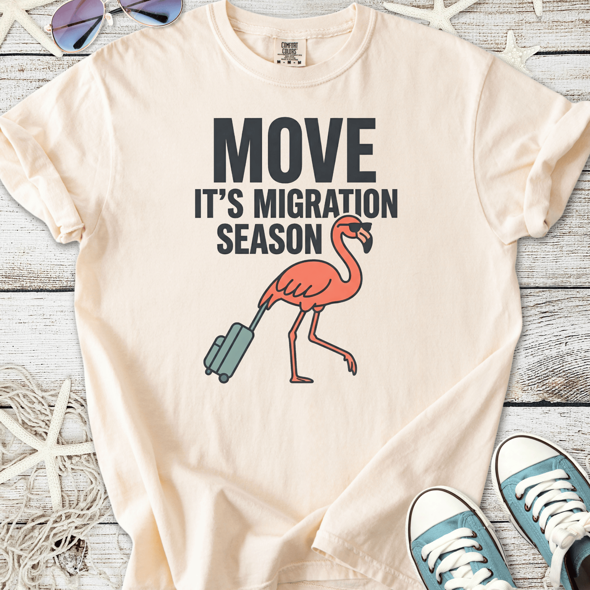 Light beige t-shirt with a fun flamingo graphic and text 'Move It's Migration Season'.