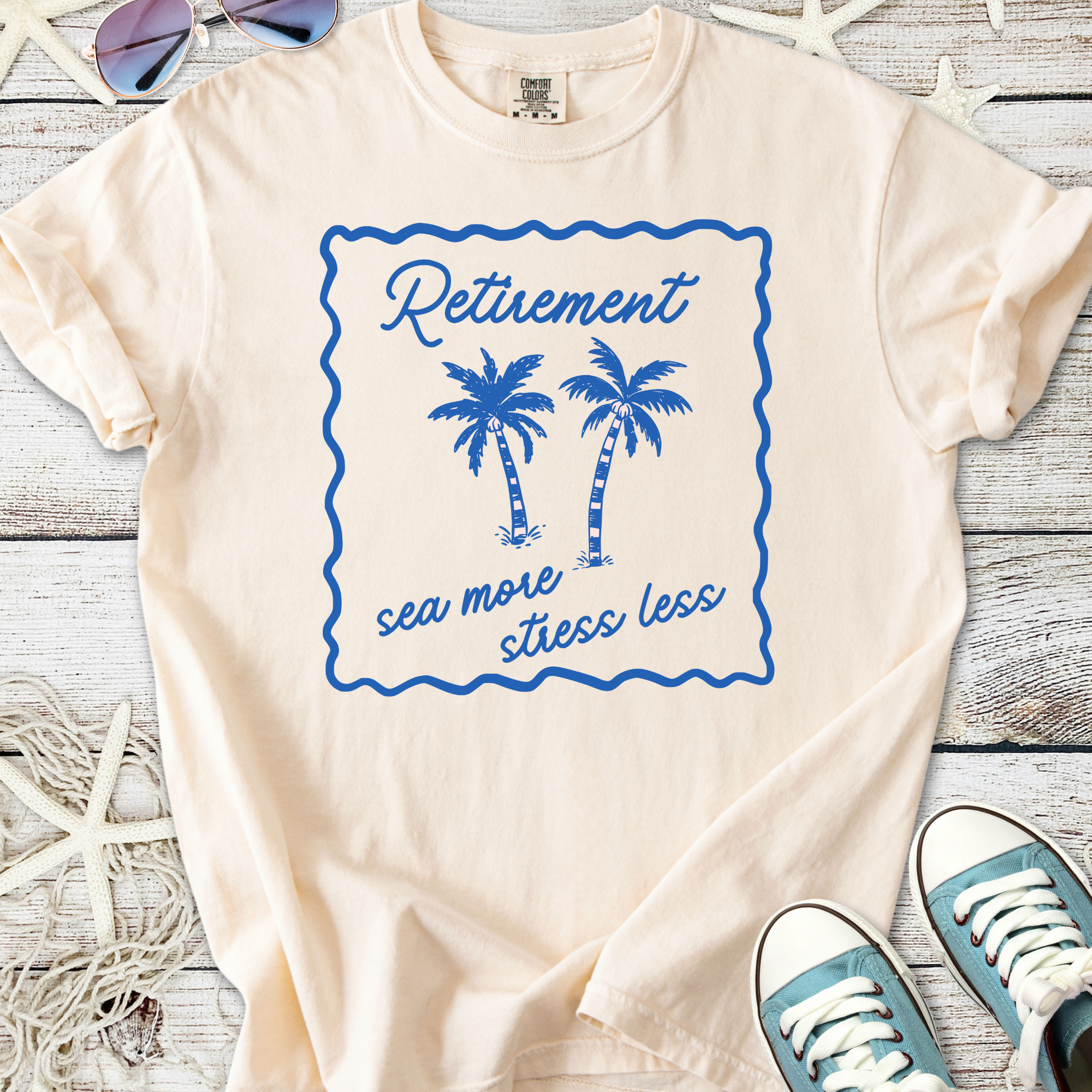 Cream retirement t-shirt with blue palm tree graphic and 'sea more stress less' slogan.