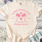 Cream t-shirt featuring pink sunset graphic with palm trees, ideal for casual summer wear.