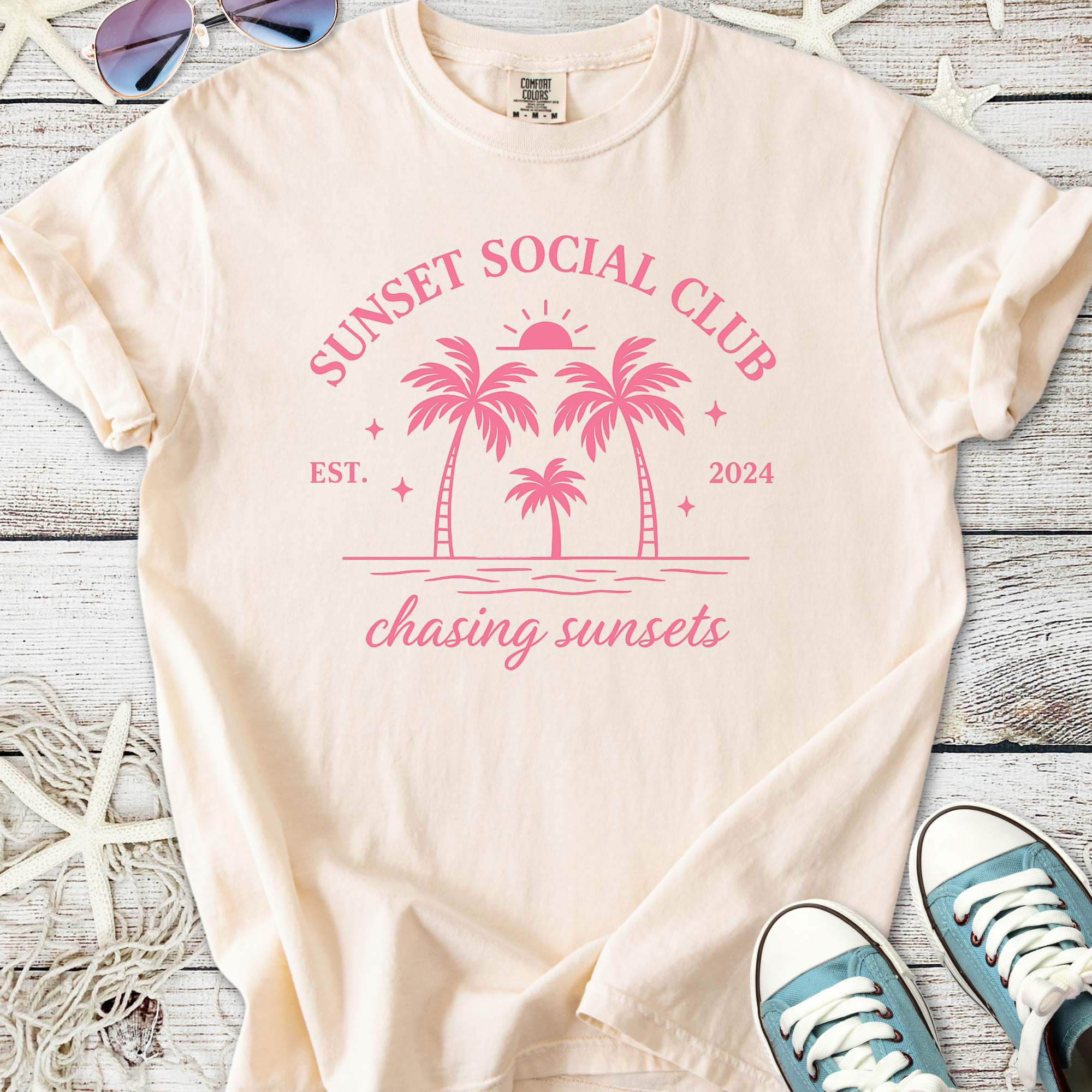 Cream t-shirt featuring pink sunset graphic with palm trees, ideal for casual summer wear.