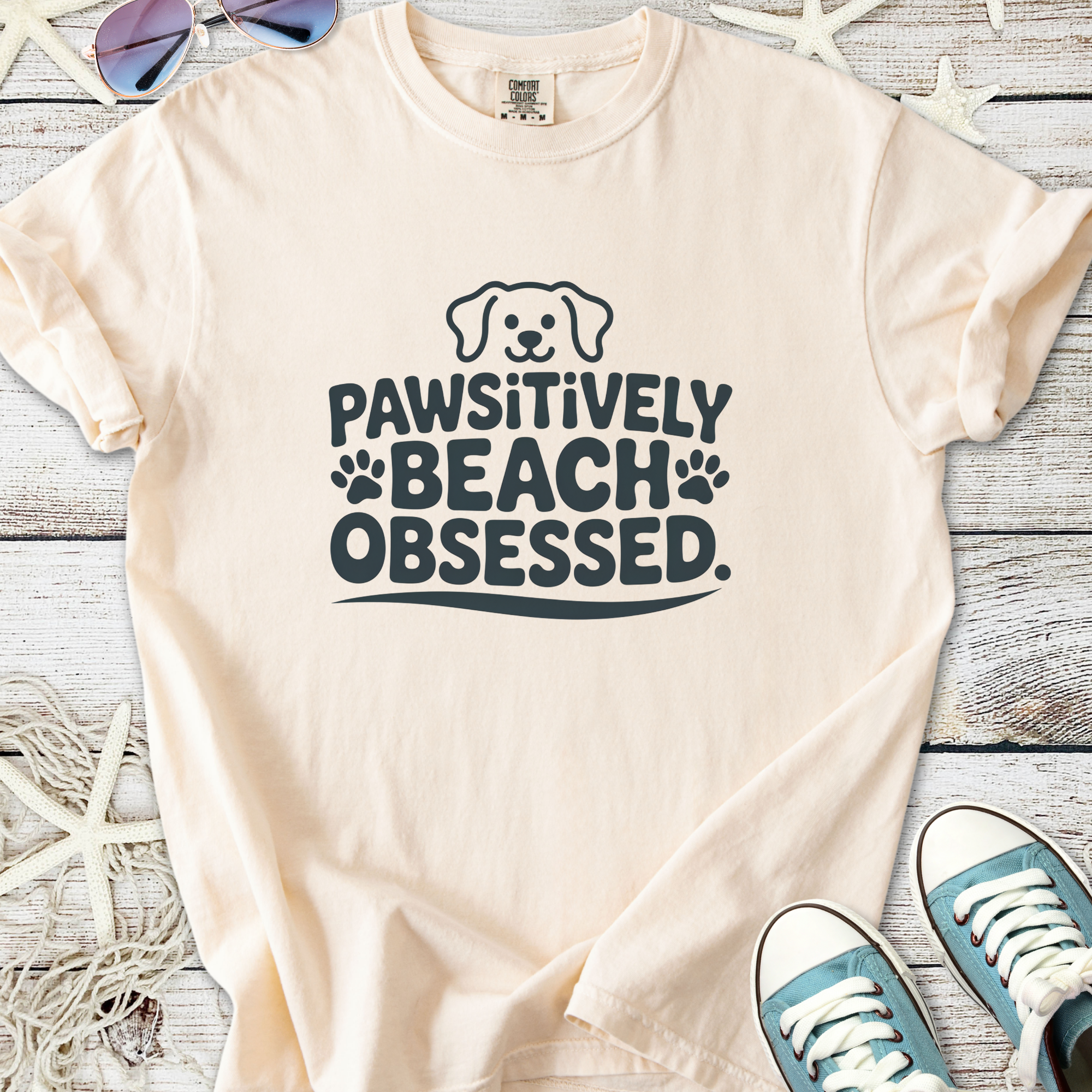 Light peach t-shirt with 'Pawsitively Beach Obsessed' graphic, perfect for dog lovers and beachgoers.