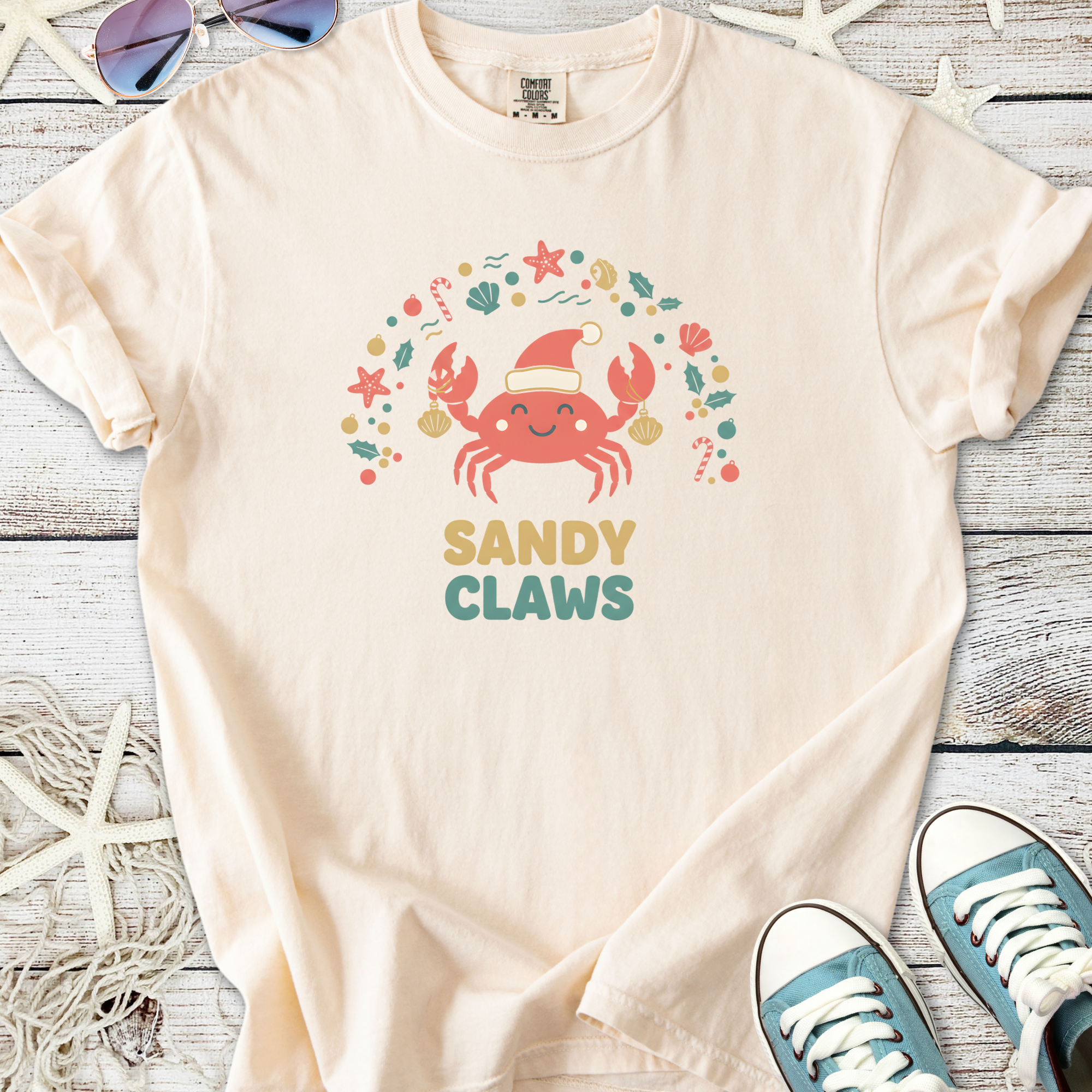 Cream t-shirt featuring a cute crab graphic with the text 'SANDY CLAWS', perfect for beach lovers.