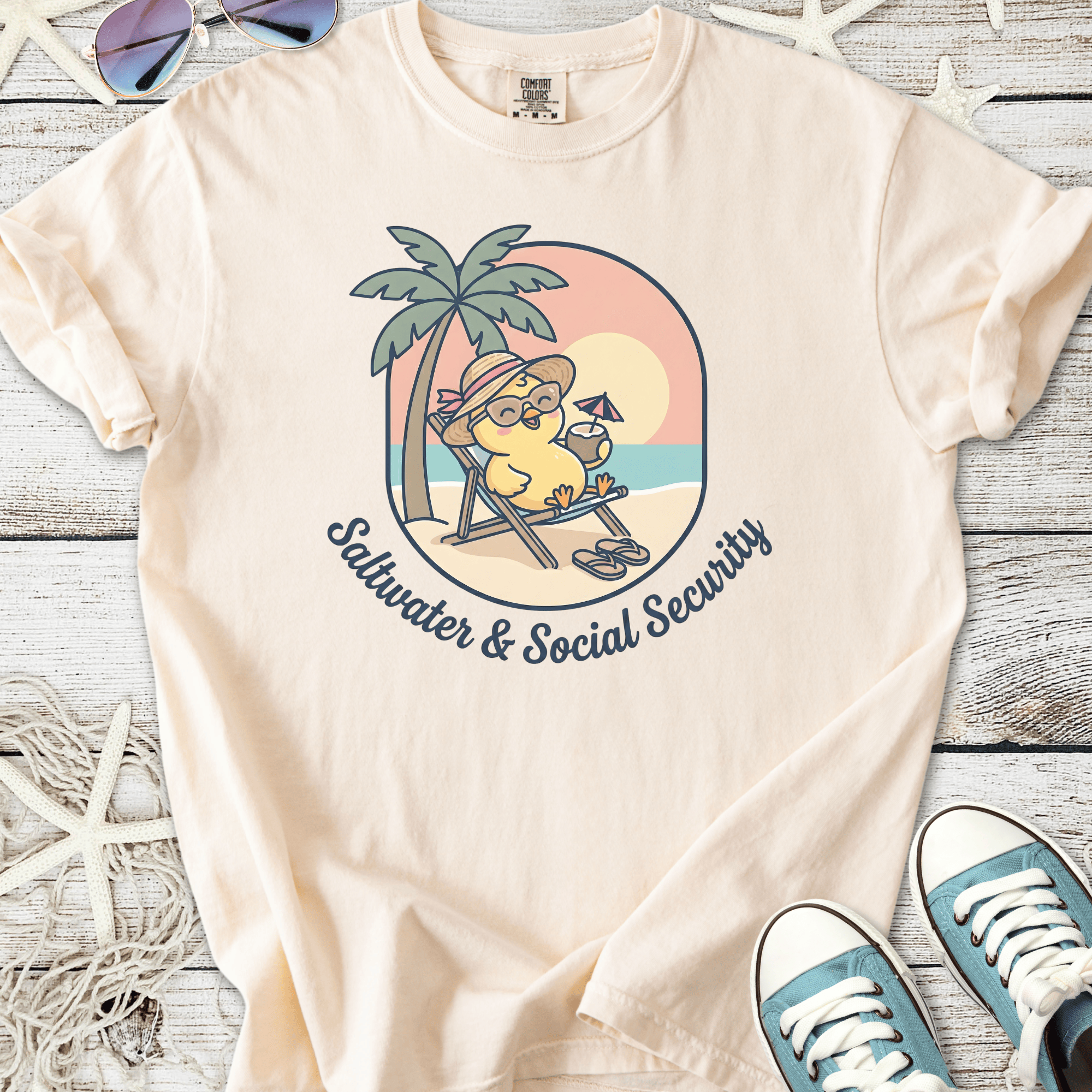 Beige cotton t-shirt featuring a cartoon character relaxing on a beach with the text 'Saltwater & Social Security'.