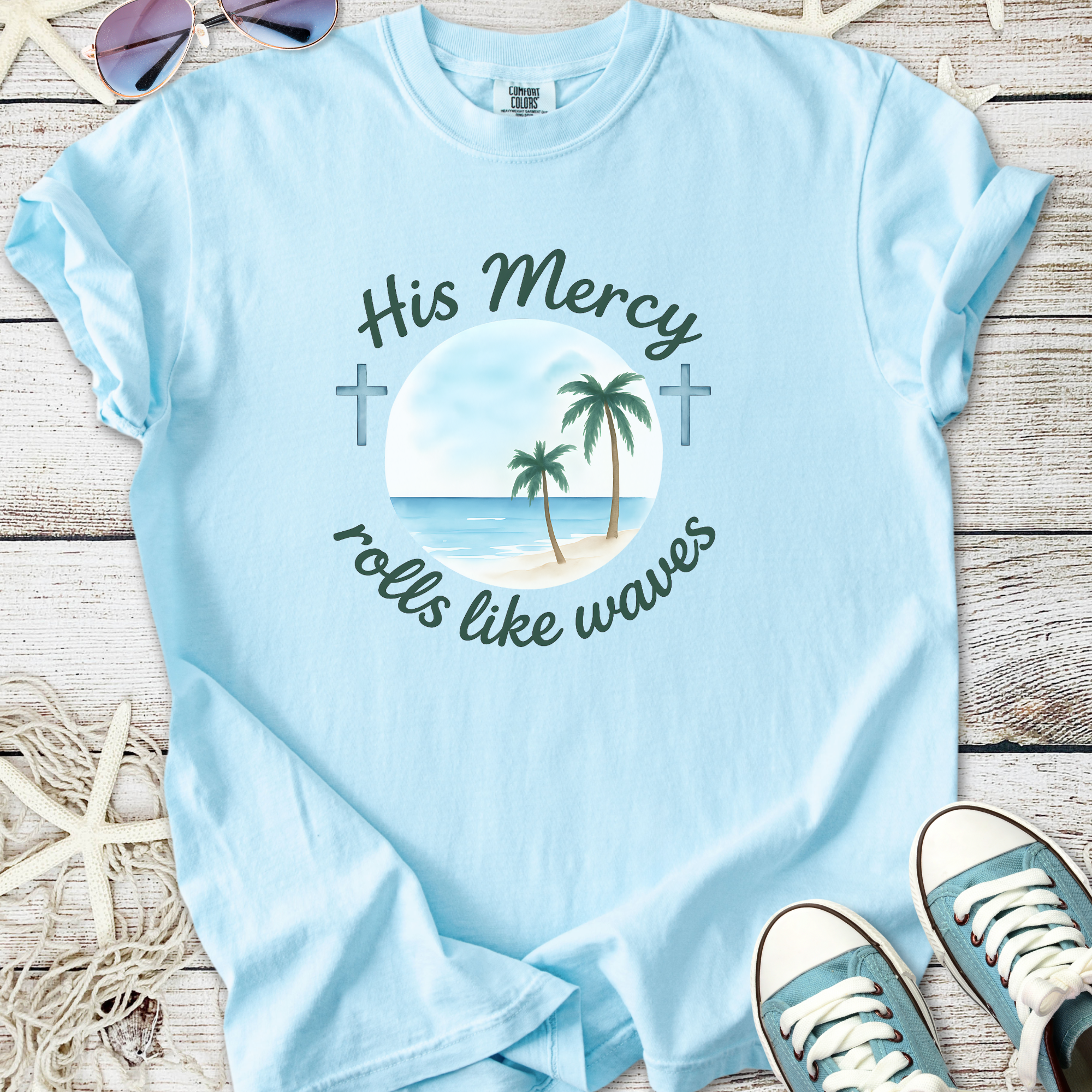 Light blue t-shirt with 'His Mercy rolls like waves' graphic and palm trees, perfect for casual wear.