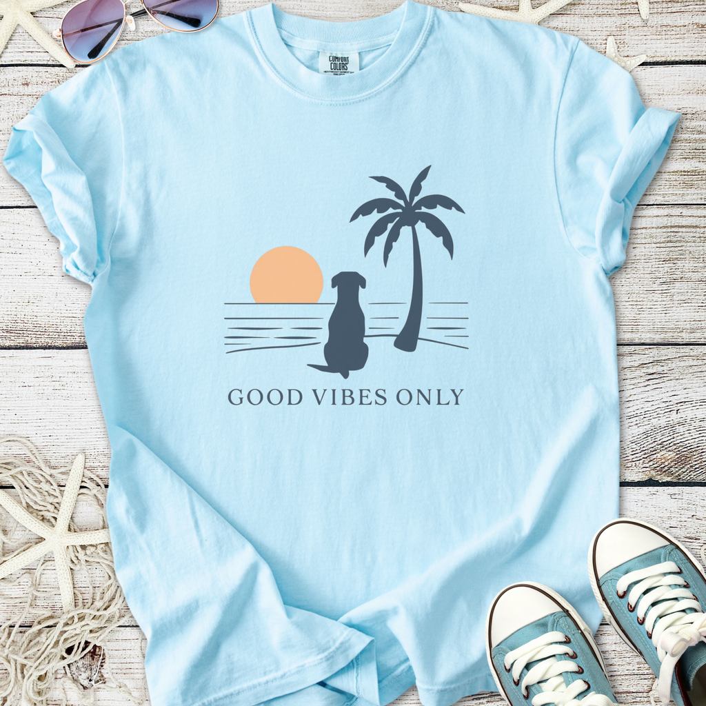 Light blue t-shirt featuring a dog, palm tree, and sunset with text 'GOOD VIBES ONLY'.