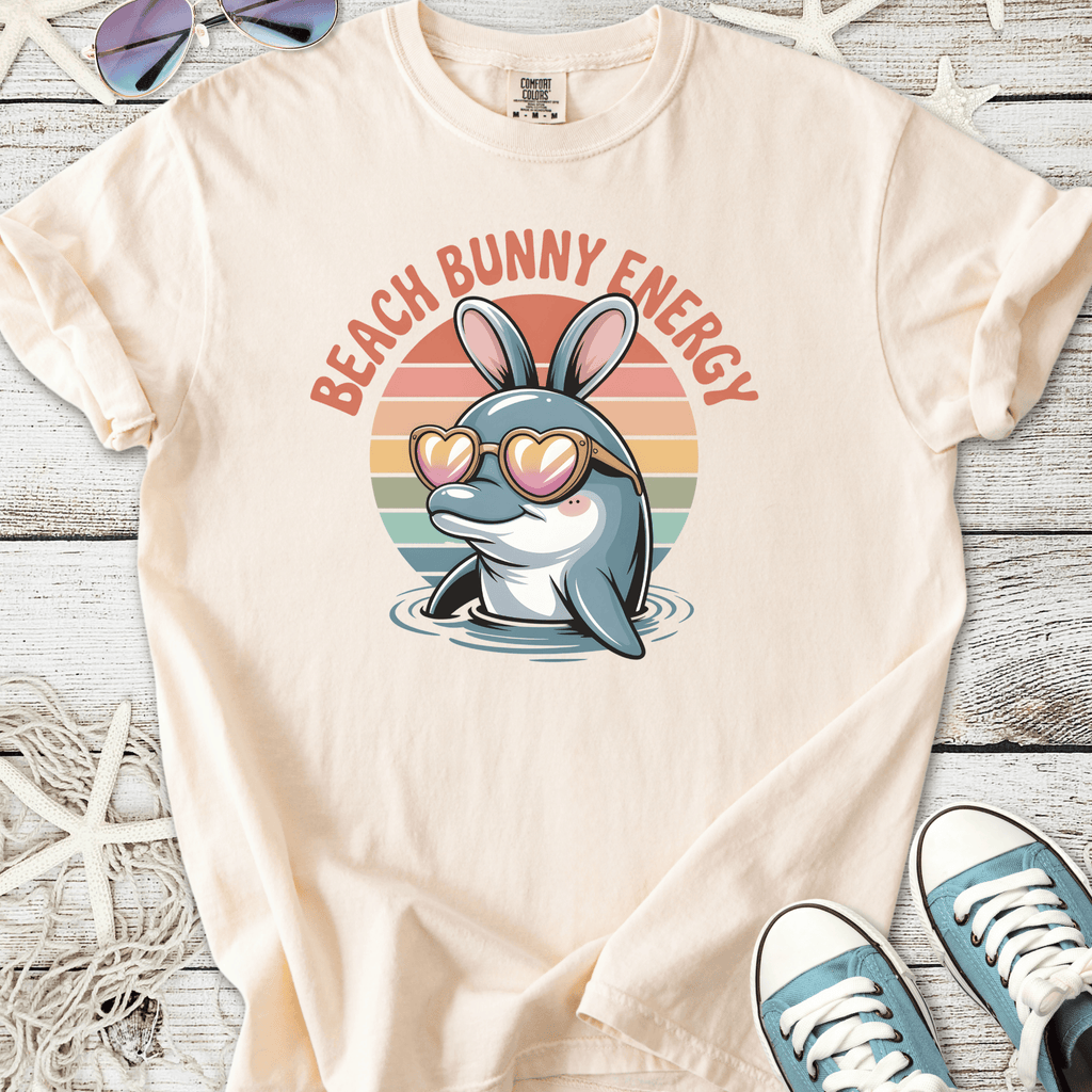 Cream t-shirt featuring a dolphin with bunny ears and heart-shaped sunglasses, text reads 'Beach Bunny Energy'.