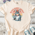 Cream t-shirt featuring a dolphin with bunny ears and heart-shaped sunglasses, text reads 'Beach Bunny Energy'.