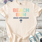 Cream cotton t-shirt with 'Beach Bum since retirement' and palm tree graphic, perfect for casual summer wear.
