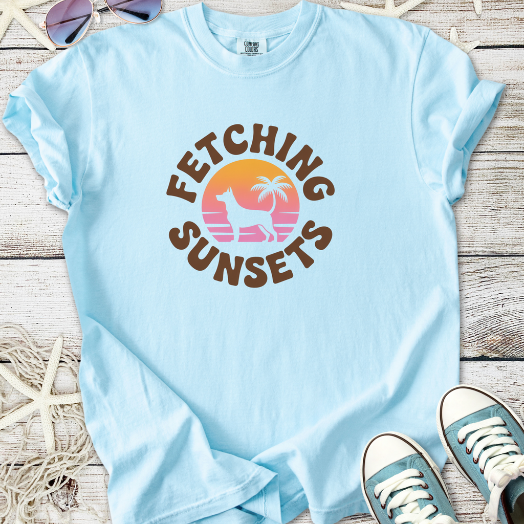 Light blue graphic tee 'Fetching Sunsets' with dog, palm tree design, perfect for casual summer wear.