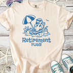 Cream t-shirt featuring a lounging flamingo with 'Retirement Plans' graphic in blue, perfect for casual wear.