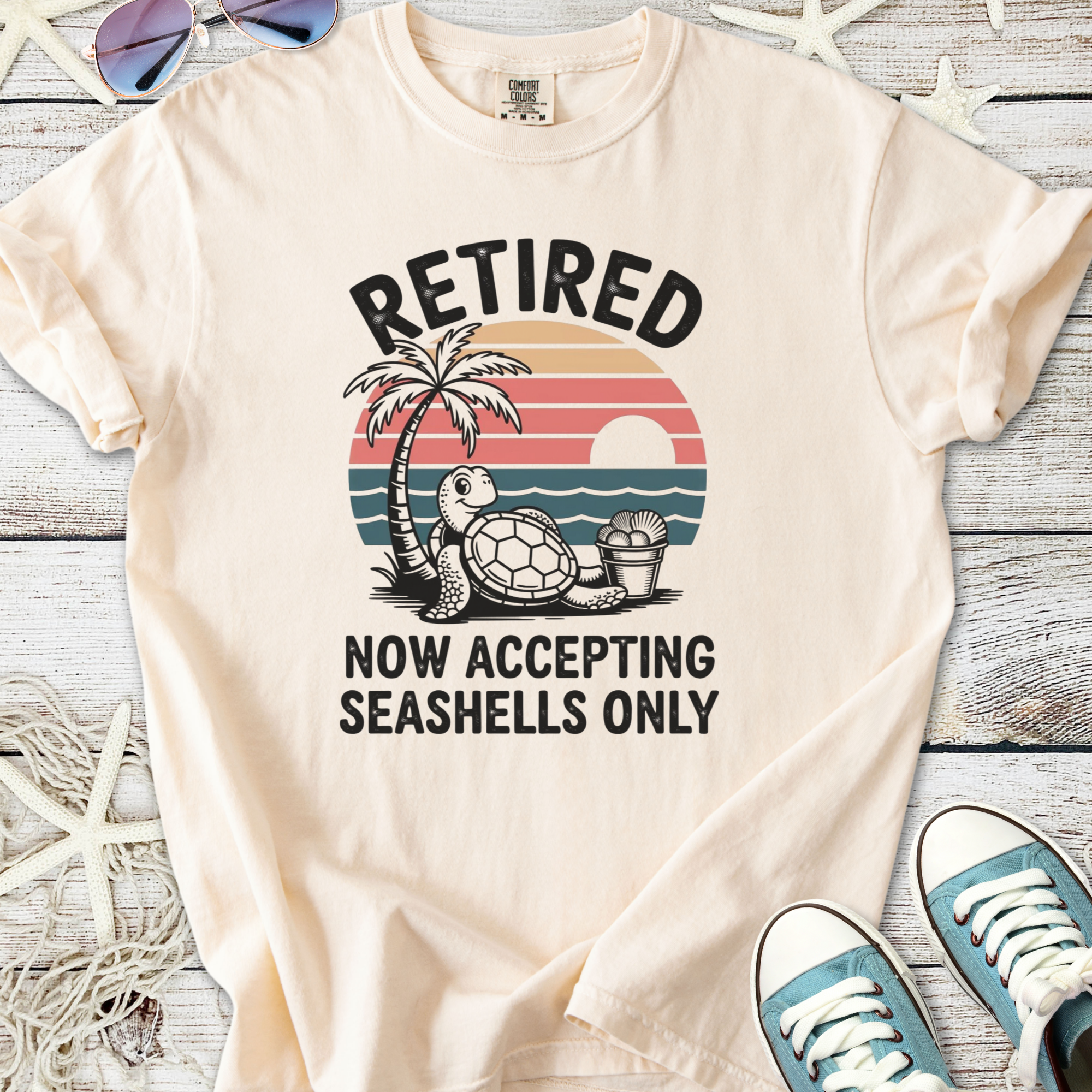 Cream t-shirt with 'Retired' graphic, turtle, palm tree, and sunset design, perfect for beach lovers.