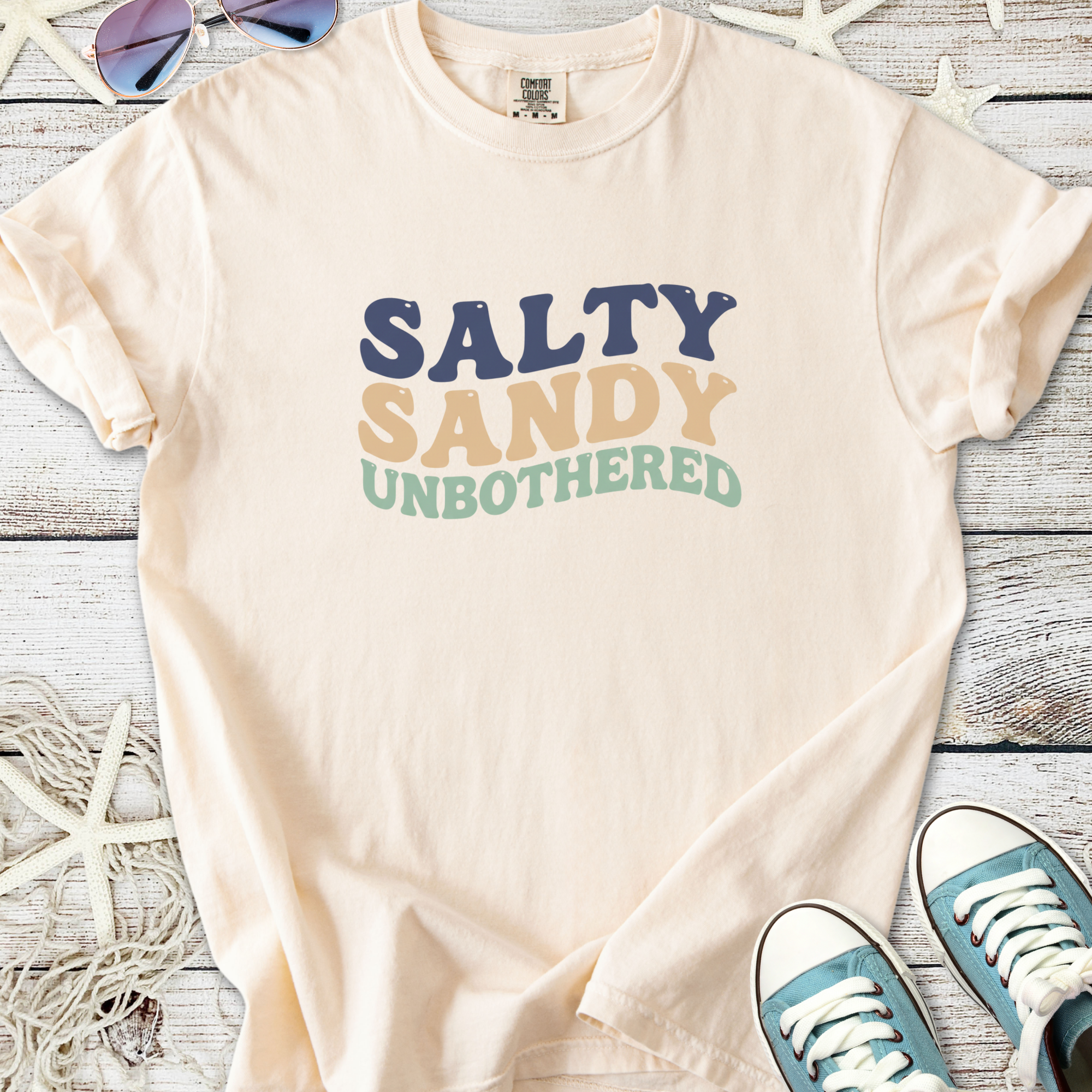 Cream t-shirt with 'Salty Sandy Unbothered' graphic, perfect for beach lovers and casual wear.