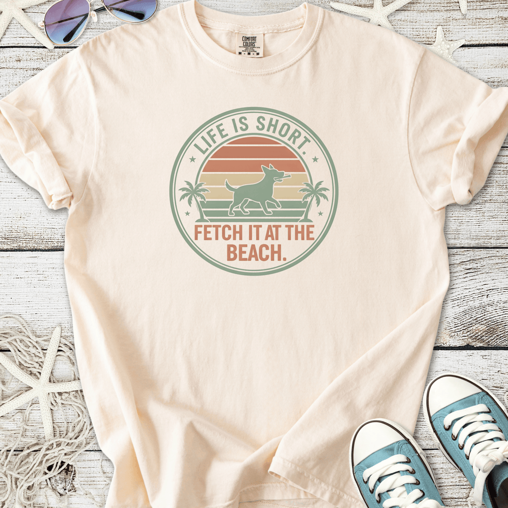 Peach t-shirt with beach-themed dog graphic, featuring 'Life is Short, Fetch It at the Beach' slogan.