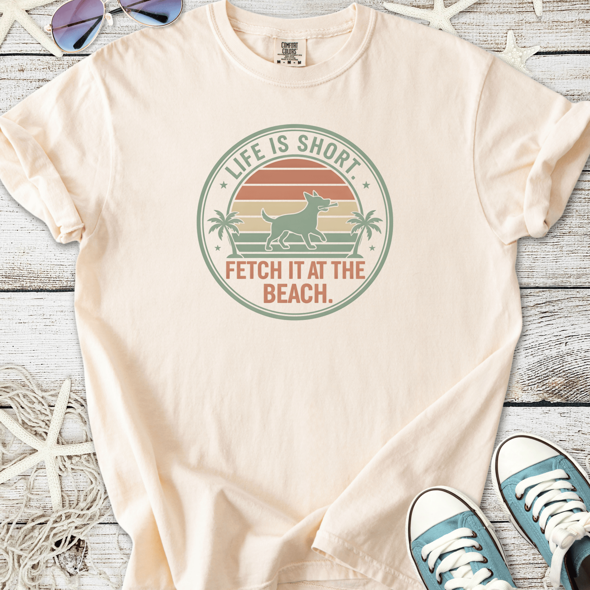 Peach t-shirt with beach-themed dog graphic, featuring 'Life is Short, Fetch It at the Beach' slogan.
