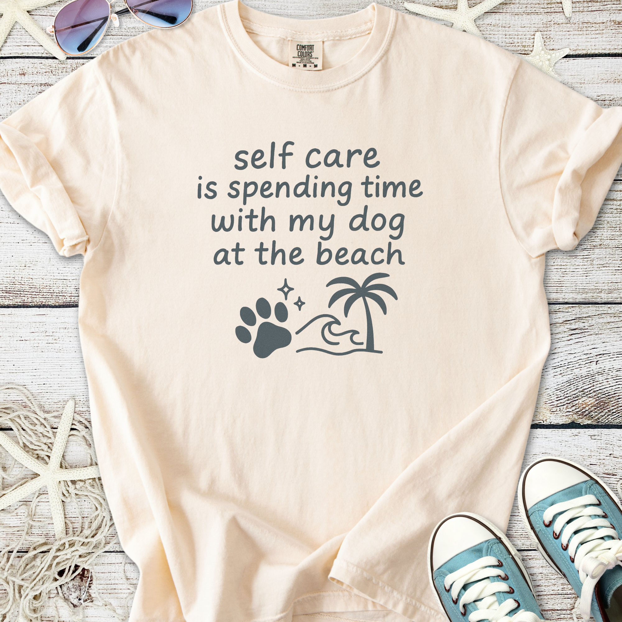 Light peach graphic tee displaying 'self care is spending time with my dog at the beach' text.