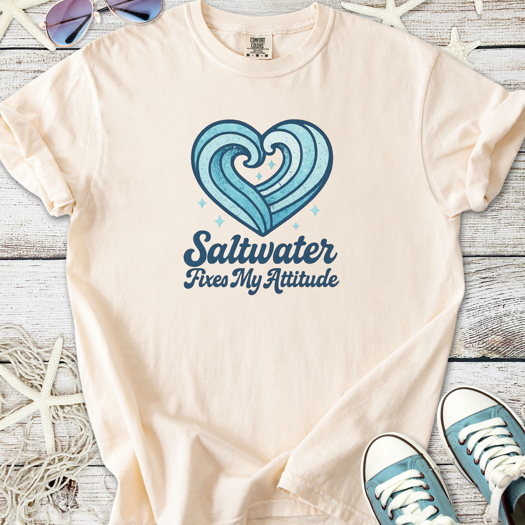 Beige graphic t-shirt with blue wave heart design and 'Saltwater Fixes My Attitude' text.