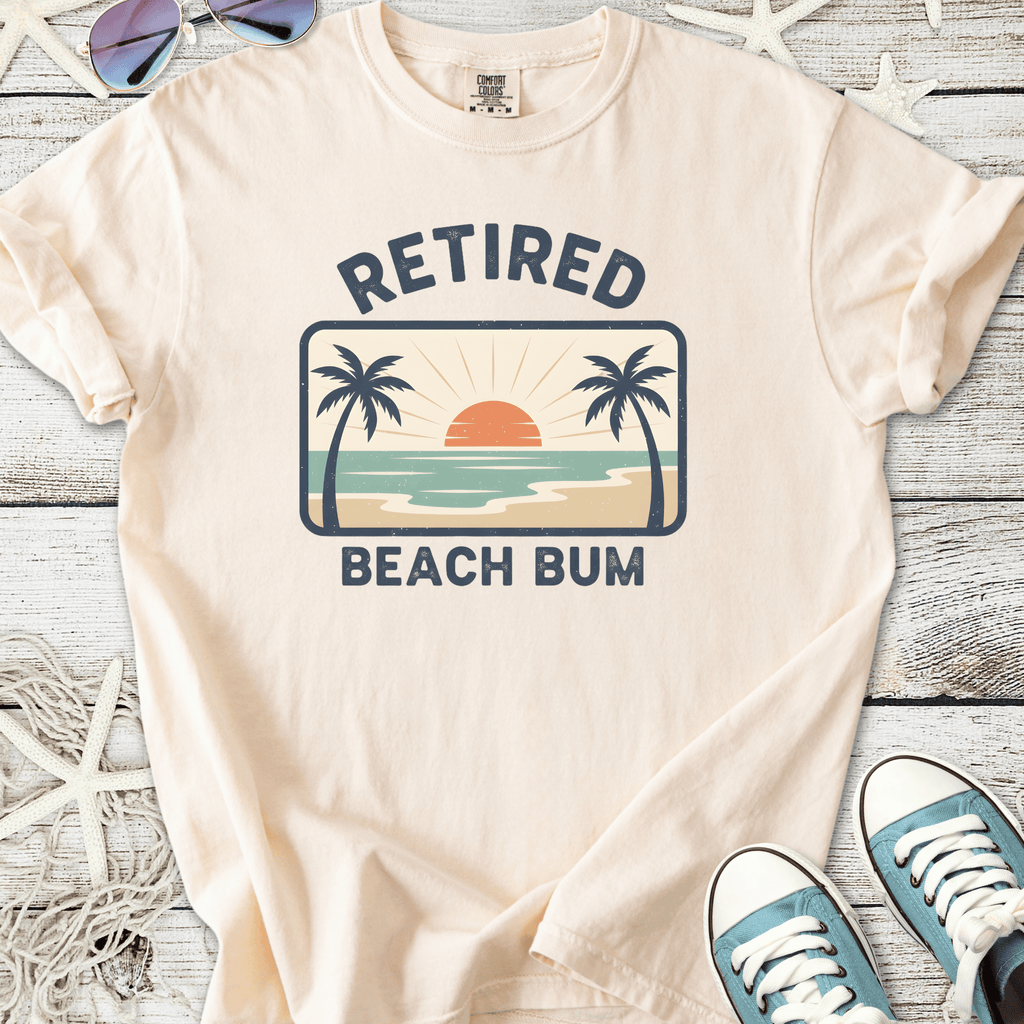 Light beige t-shirt with 'Retired Beach Bum' graphic, featuring a sunset and palm trees.