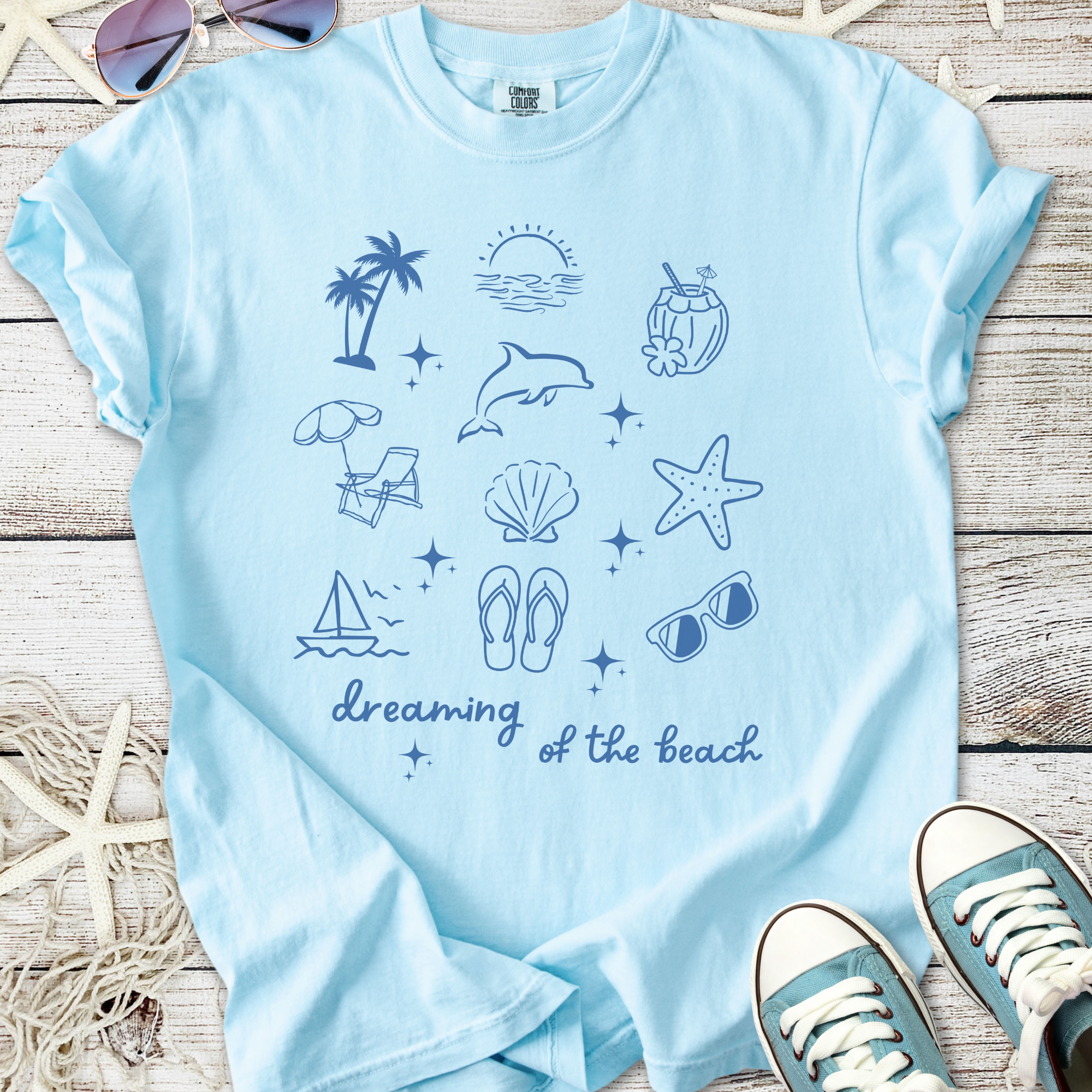 Light blue t-shirt featuring beach-themed graphics and the phrase 'dreaming of the beach'.