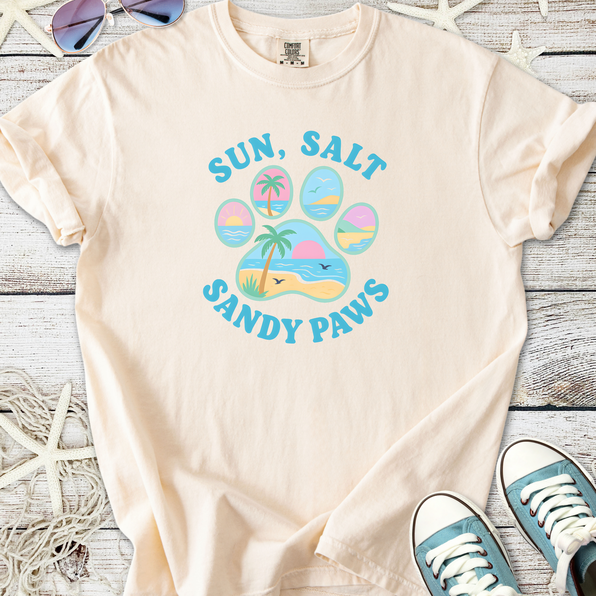 Light beige t-shirt with 'Sun, Salt, Sandy Paws' graphic, perfect for beach lovers and pet enthusiasts.