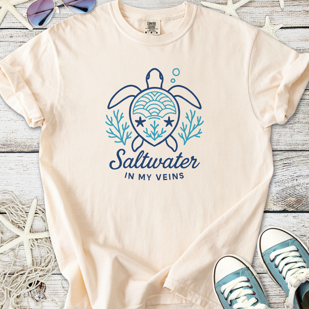 Light beige t-shirt with a turtle graphic and 'Saltwater in My Veins' text, made from soft cotton material.