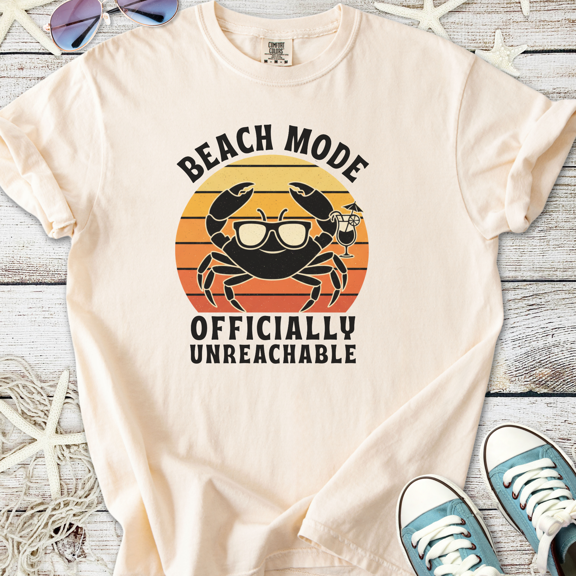 Cream beach-themed t-shirt featuring a crab graphic with sunglasses, stating 'Beach Mode - Officially Unreachable'.