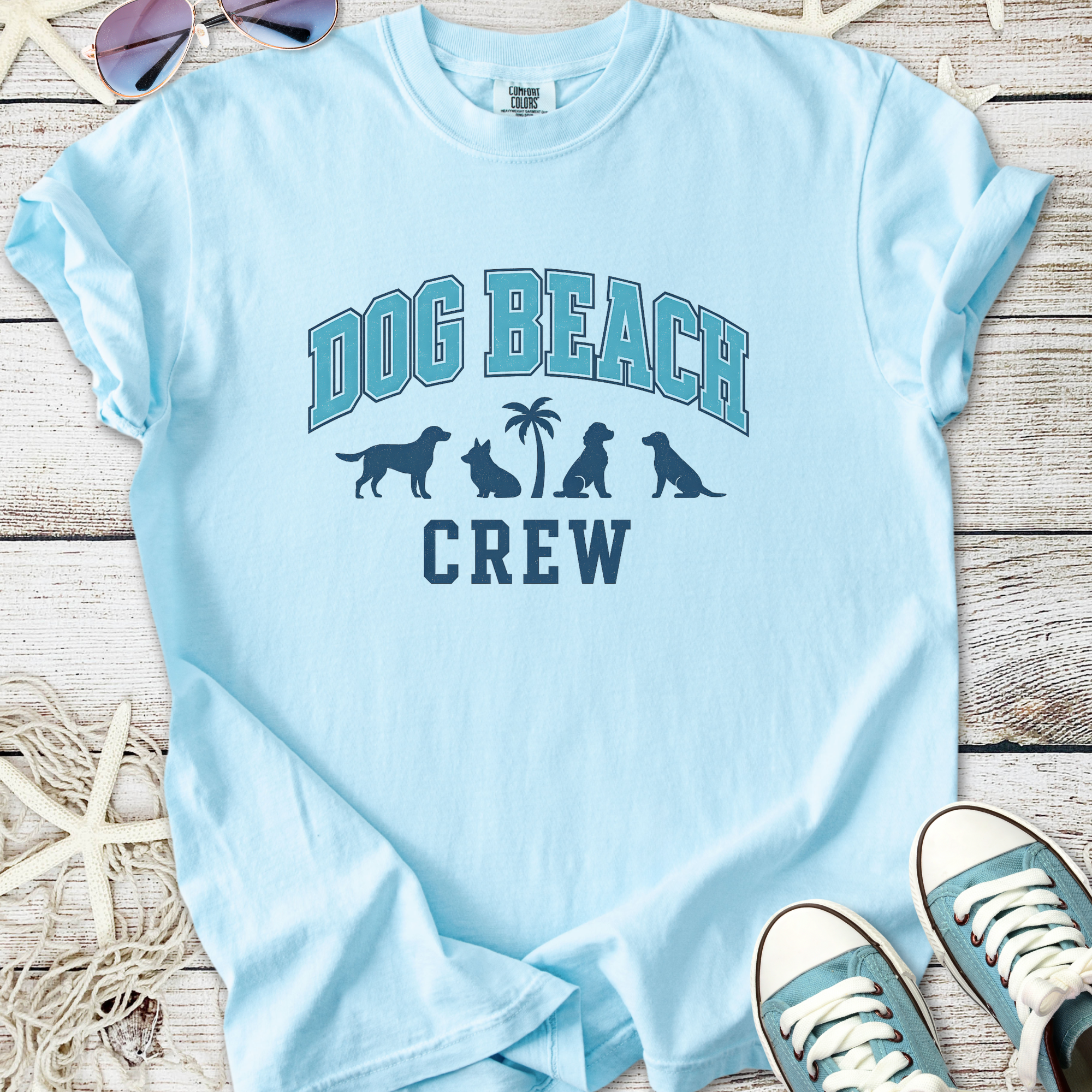 Light blue t-shirt with 'Dog Beach Crew' graphic and dog silhouettes, perfect for beach outings.