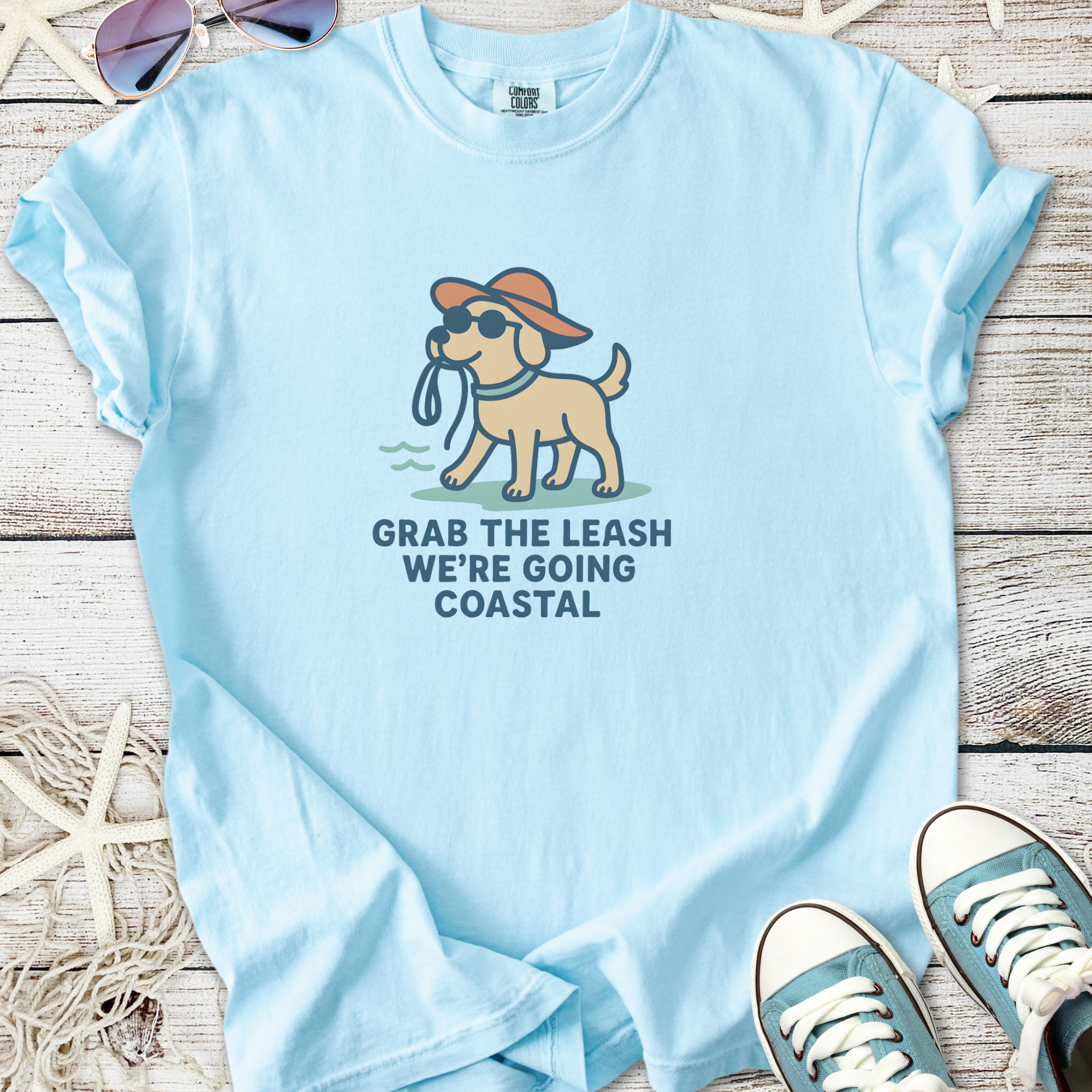Light blue unisex t-shirt featuring a dog with sunglasses and a hat, text: 'Grab the leash, we’re going coastal'.