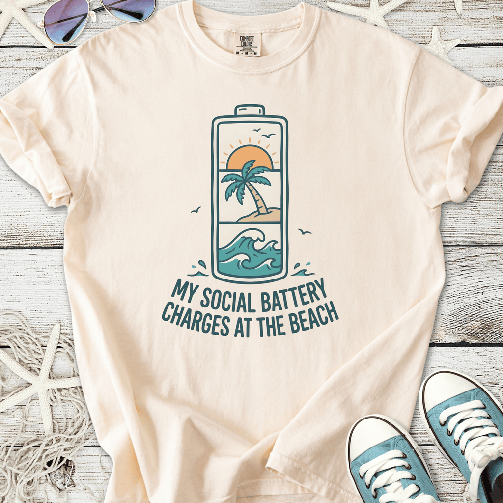 Cream graphic t-shirt featuring beach-themed design, 'My Social Battery Charges at the Beach'.