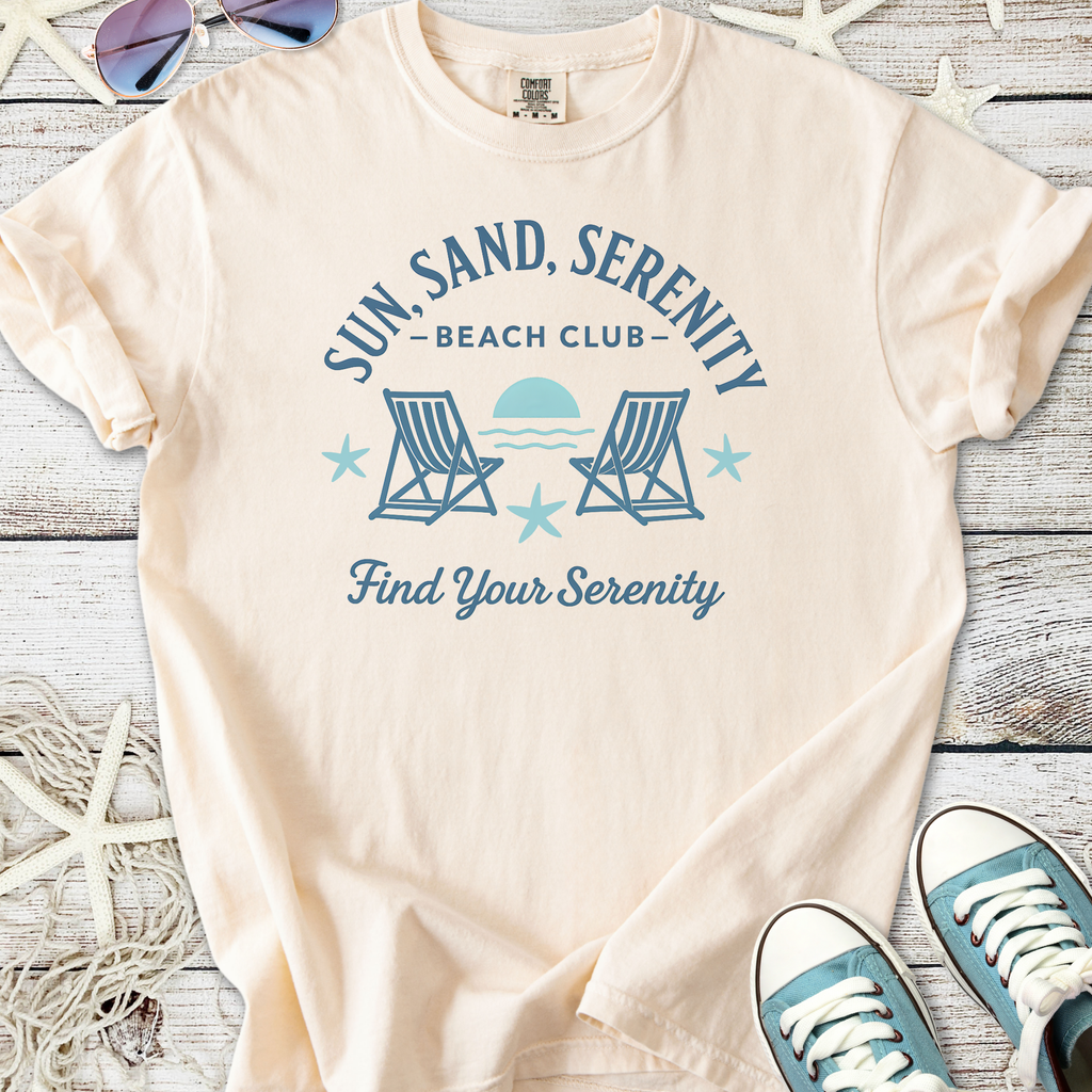 Beige cotton t-shirt with 'Sun, Sand, Serenity Beach Club' graphic and lounge chairs design.