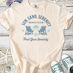 Beige cotton t-shirt with 'Sun, Sand, Serenity Beach Club' graphic and lounge chairs design.