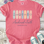 Pink graphic t-shirt featuring 'Anchored in Faith' design with icons, made from soft cotton.