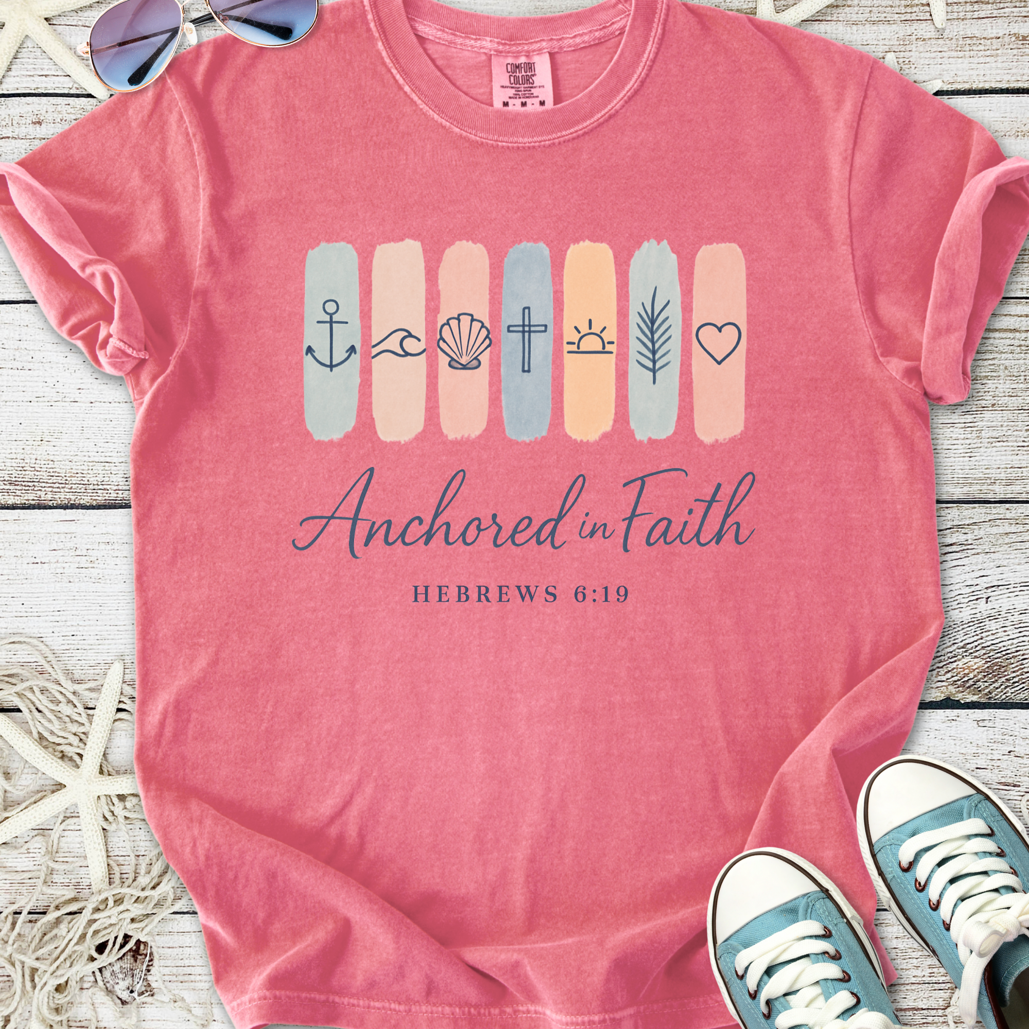 Pink graphic t-shirt featuring 'Anchored in Faith' design with icons, made from soft cotton.