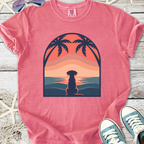 Pink graphic tee featuring a silhouette of a dog by the beach at sunset, made from soft cotton.