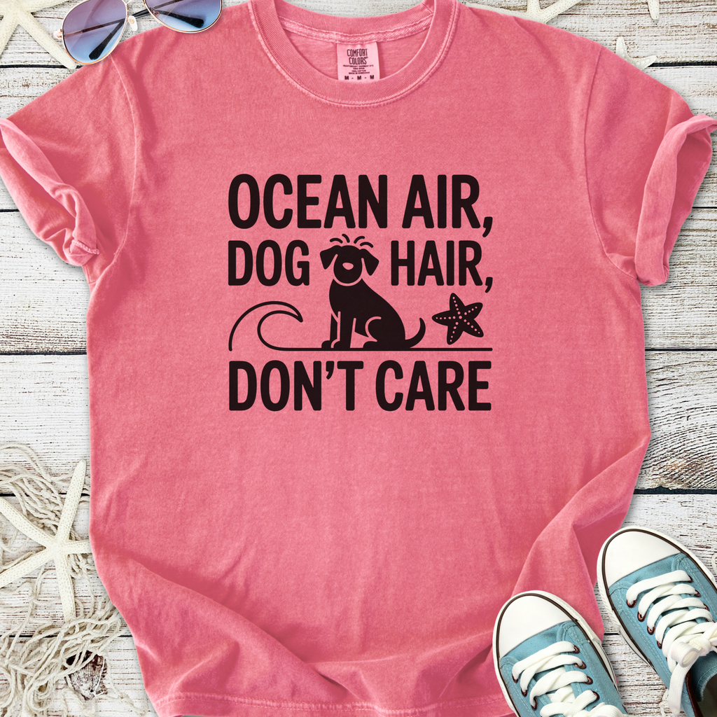 Pink graphic tee with 'Ocean Air, Dog Hair, Don't Care' text and dog design, perfect for beach lovers.