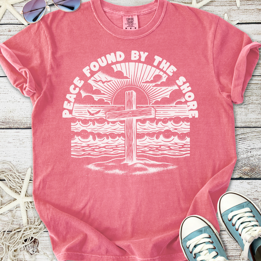 Pink graphic t-shirt featuring a cross and beach design, perfect for coastal vibes and casual wear.