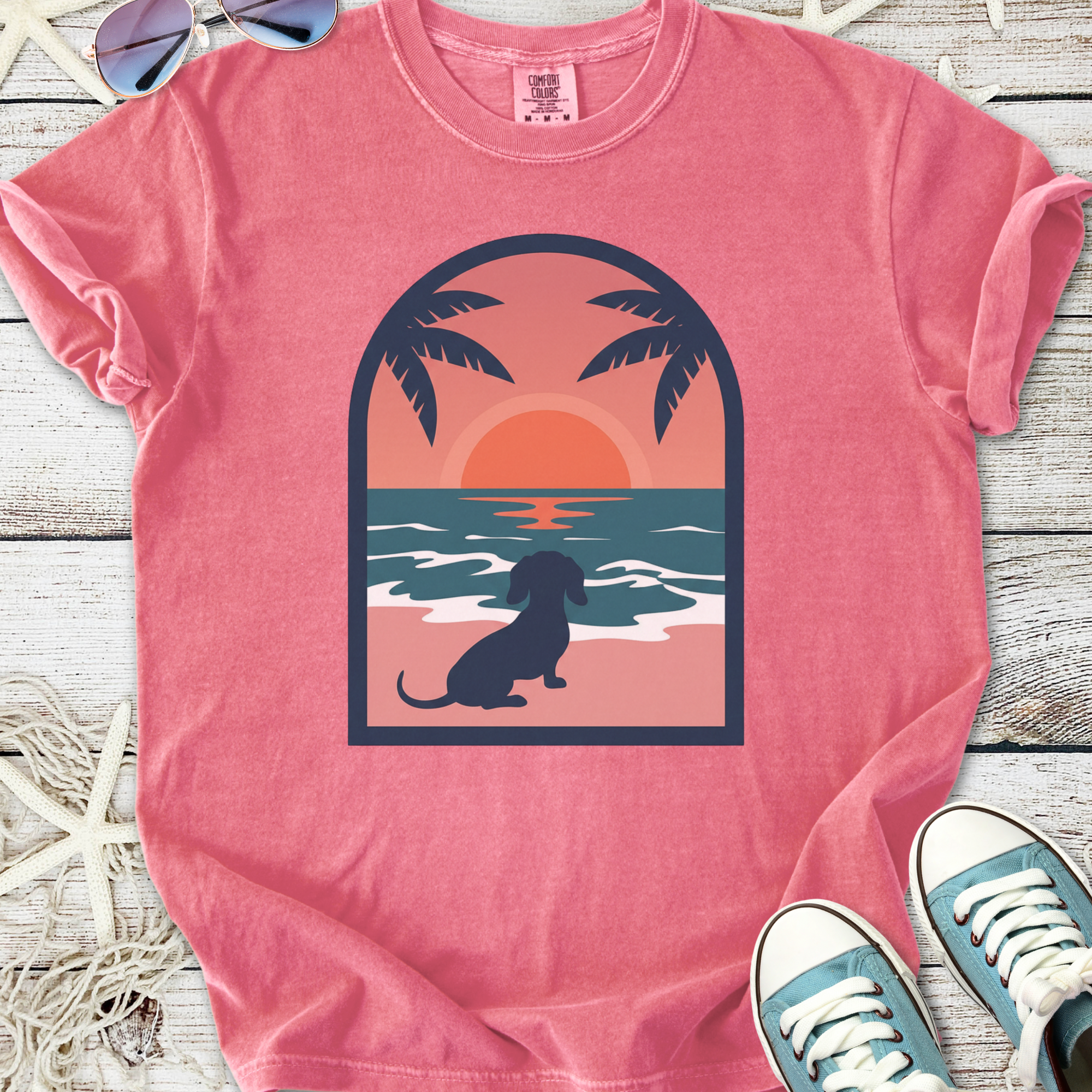 Pink graphic tee featuring a dog silhouette, sunset, and palm trees, perfect for casual beach vibes.